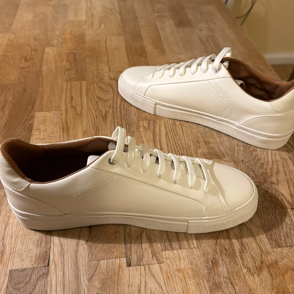 Säljer ett par stilrena vita sneakers från Zara i nytt skick. De har en klassisk design med snörning och är perfekta för både vardag och fest. Skorna är gjorda i syntetmaterial och har en bekväm passform. Perfekta för vår och sommar! . Skor.