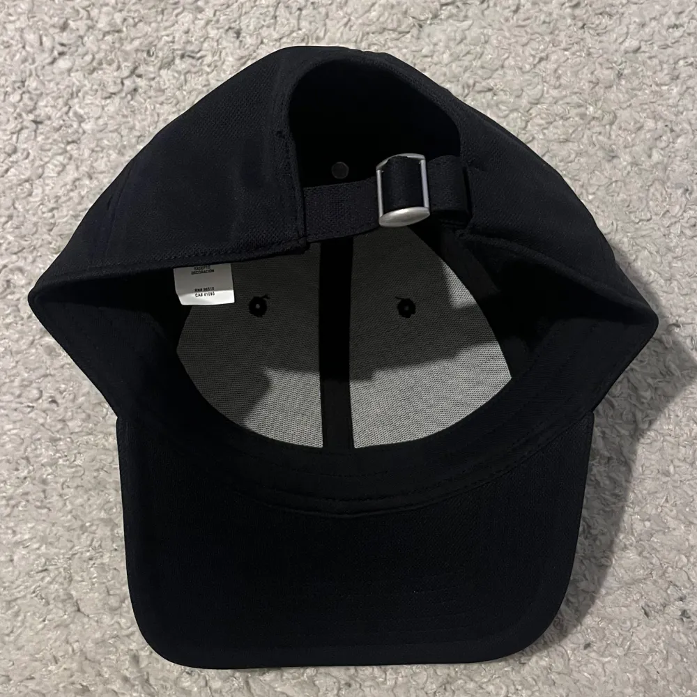 Säljer en snygg svart keps från Under Armour i nytt skick. Kepsen har en justerbar rem baktill för perfekt passform och är tillverkad i bomull. Perfekt för både vardag och träning!. Asusteet.