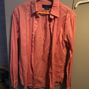 Rosa skjorta från Ralph Lauren - Säljer en snygg rosa skjorta från Ralph Lauren i slim fit. Skjortan är långärmad och har klassiska knappar framtill. Den är i bomull och har en broderad logga på bröstet. Perfekt för både vardag och fest!Cond:9/10. Pris kan diskuteras vid snabb affär!🔥