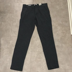 Mörkblå byxor från Jack & Jones - Säljer ett par mörkblå byxor från Jack & Jones i modellen Slim Marco. De har en slim passform och är perfekta för både vardag och fest. Byxorna har en diskret mönstring och stängs med dragkedja och knappar. De är i mycket bra skick och redo för en ny ägare!