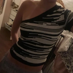 Svartvit randig oneshoulder topp - Säljer en supercool svartvit randig oneshoulder topp. Den är tight och perfekt för en utekväll eller fest. Materialet är mjukt och stretchigt, vilket gör den bekväm att bära hela dagen. Passar perfekt till jeans eller kjol för en trendig look!
