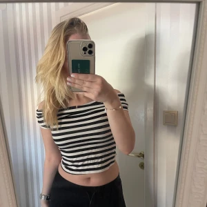 Randig croppad topp - Säljer en superfin randig topp i svart och vit. Den är croppad och har korta ärmar, perfekt för sommardagar. Toppen är i bra skick och passar till både vardag och fest. Den är off shoulder