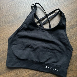 Svart sporttopp från Astani - Säljer en svart sporttopp från Astani i mycket bra skick. Den har en snygg design med korsade band i ryggen och är tillverkad i ett mjukt och stretchigt material. Perfekt för träning eller en aktiv vardag!