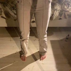 Beige cargopants med fickdetaljer - Säljer ett par snygga beige cargopants i bra skick. De har en normal passform och är perfekta för höst och vår. Byxorna har flera praktiska fickor med knappar och en dragkedja framtill. Materialet känns slitstarkt och bekvämt. Perfekta för en avslappnad stil!