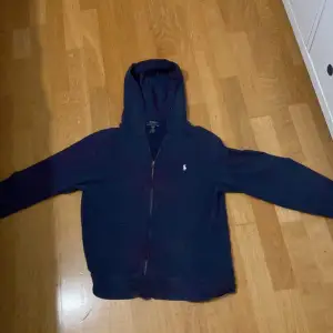 Säljer en snygg mörkblå hoodie från Ralph Lauren i storlek XL barn som är som storlek xs-s Den har en dragkedja framtill och den klassiska loggan broderad på bröstet. Perfekt för höst och vinter, och den är i mycket bra skick. Kan gå ner i pris vid snabb affär 