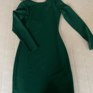 Mörkgrön klänning - Snygg mörkgrön klänning i ett stilrent och elegant snitt. Den har långa ärmar och en u ringning i ryggen som ger en klassisk look. Perfekt för höst- och vinterfester eller en elegant middag. 