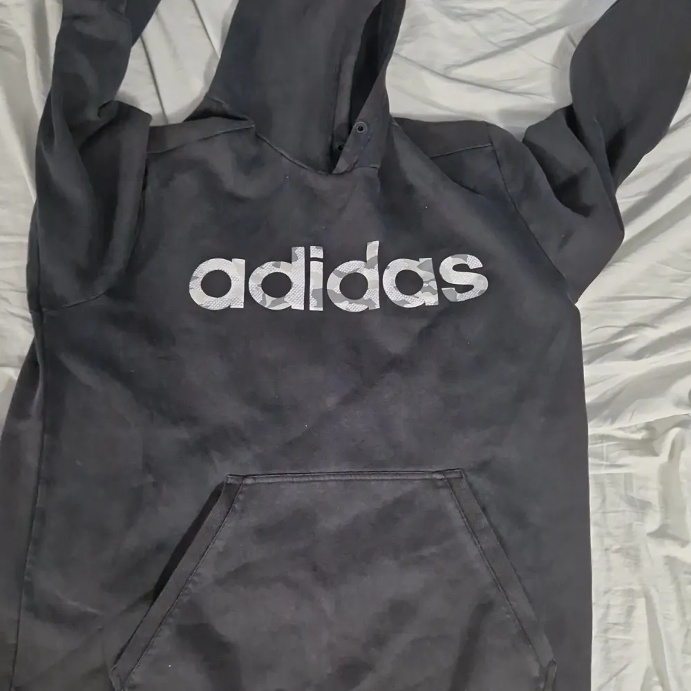 Säljer en svart hoodie från Adidas i bra skick. Den har en stor logga på framsidan och en praktisk magficka. Perfekt för höst och vinter, och den är superbekväm att ha på sig. Passar både till vardags och träning!. Tröjor & Koftor.