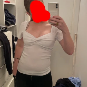 Vit topp med korta ärmar - Säljer en söt vit topp med korta ärmar och en fin v-ringad design. Toppen har en tight passform och är perfekt för både vardag och fest. Den är i mycket bra skick och passar bra till jeans eller kjol.