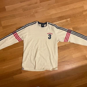 Beige långärmad tröja från Adidas - Säljer en beige långärmad tröja från Adidas med röda och svarta detaljer. Den är i bra skick, säljer då den inte kommer till användning längre 💞