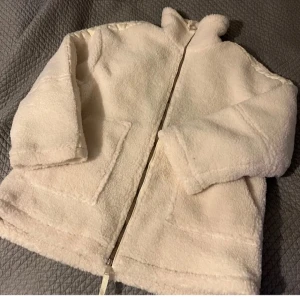 Vit teddyjacka med dragkedja - Mysig vit teddyjacka i mycket bra skick. Perfekt för kyliga höst- och vinterdagar. Jackan har en dragkedja framtill och två fickor. Insidan är quiltad för extra värme och komfort. Säljer då den var lite för stor! (Lånade bilder) skriv för egna bilder
