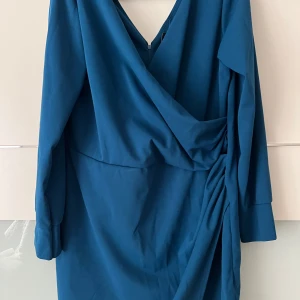 Omlottklänning i blått och gult - Snygg omlottklänning i två färger: en i djupblå och en i senapsgul. Klänningarna har långa ärmar och en elegant drapering på sidan. Perfekt för både vardag och fest!