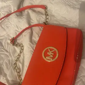 Snygg orange axelväska från Michael Kors i skinn med guldfärgad kedja och logotyp. Perfekt för att liva upp vilken outfit som helst! Väskan är i mycket bra skick och har en stilren design som passar både till vardags och fest.