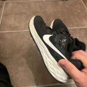 Svarta Nike sneakers - Säljer ett par svarta Nike sneakers i bra skick. De har en vit sula och klassisk Nike-logga på sidan. Perfekta för träning eller vardagsbruk. Lite slitage på ovansidan men inget som påverkar funktionen. Sköna och lätta att bära!