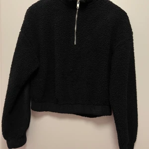 Svart fleece tröja från Gina Tricot - Mysig svart fleece tröja från Gina Tricot i storlek S. Perfekt för kyliga dagar med sin mjuka och varma känsla. Tröjan har en halv dragkedja framtill och långa ärmar. Passar perfekt för både vardag och mysiga hemmakvällar.