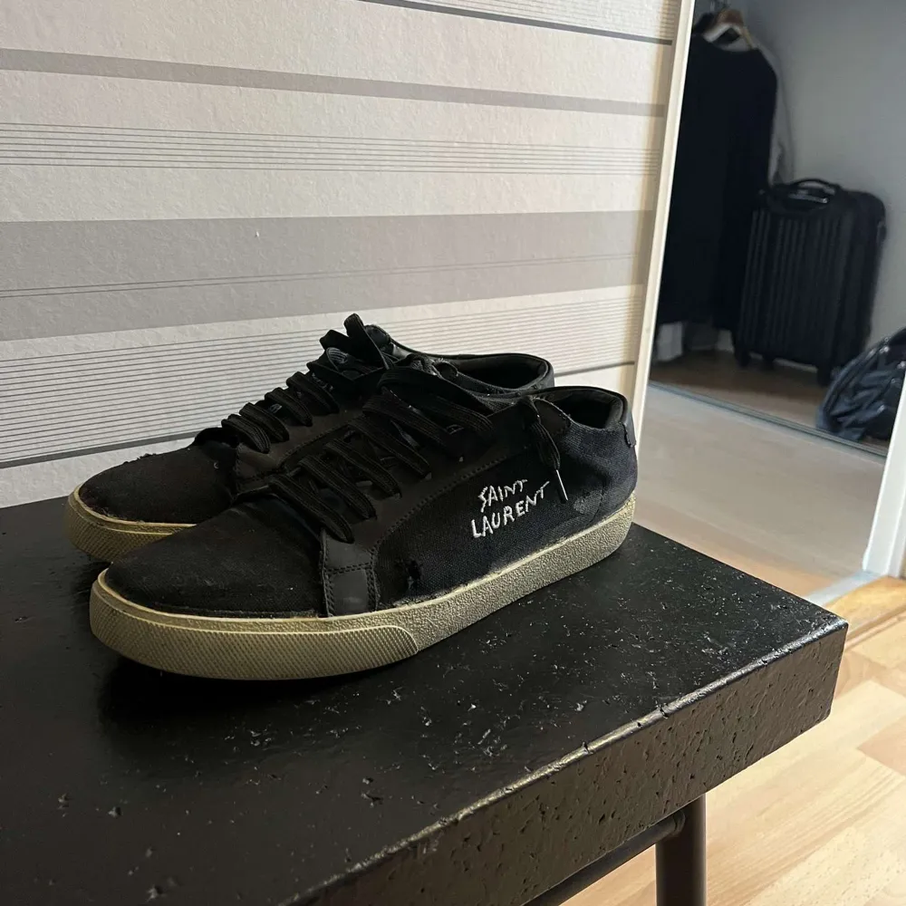 Säljer ett par svarta sneakers från Saint Laurent i bra skick. De har en klassisk design med snörning och vit sula. Perfekta för både vardag och fest. Har inget og. Skor.