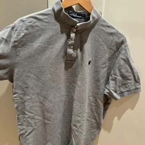 Grå pikétröja från Ralph Lauren - Säljer en klassisk grå pikétröja från Ralph Lauren i storlek L. Tröjan är i bomull och har korta ärmar med en liten broderad logga på bröstet. Perfekt för en avslappnad men stilren look. Passar både till vardags och lite finare tillfällen. Nypris ca 1000kr