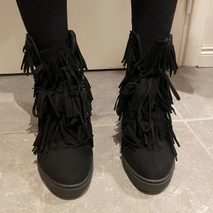 Svarta boots med fransar - Säljer ett par svarta boots i syntetmaterial med coola fransdetaljer. De har en bekväm passform och är perfekta för höst och vinter. Skorna har en diskret klack och är i mycket bra skick. Storlek 37, skriv om du har frågor!