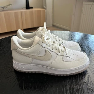 Vita Nike Air Force 1 - Säljer ett par klassiska vita Nike Air Force 1 i skinn. De har en stilren design med snörning och den ikoniska swoosh-loggan på sidan. Perfekta för både vardag och fest! Skorna är i mycket bra skick och redo för en ny ägare.