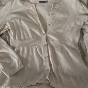 Beige kofta från Åhléns - Säljer en superfin beige kofta från Åhléns i storlek M. Den har långa ärmar och knappar framtill. Perfekt för både vår och höst, och den är i bra skick. Passar till alla tillfällen! 🌟