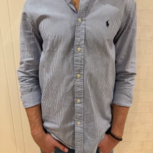 Randig skjorta från Ralph Lauren - Säljer en snygg och klassisk blå- och vitrandig skjorta från Ralph Lauren. Skjortan har långa ärmar och knappar framtill. Perfekt för både vardag och fest! 🕺