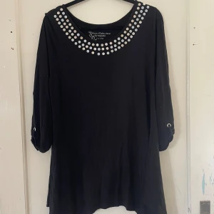 Svart topp med nitar från KappAhl - Säljer en svart topp från KappAhls Women's Collection. Den har coola silverfärgade nitar runt halsringningen och trekvartsärmar med en liten detalj vid ärmsluten. Perfekt för en avslappnad men ändå stilren look.