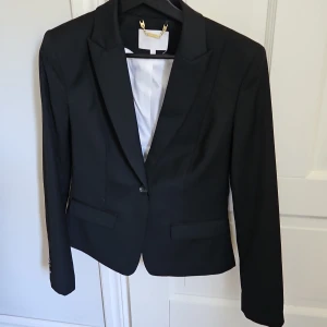 Svart kavaj med vit foder - Säljer en stilren svart kavaj med vit foder. Den har en klassisk design med en knapp framtill och långa ärmar. Perfekt för både formella och semi-formella tillfällen. Knappt använd.