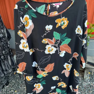 Blommig klänning från Indiska - Säljer en superfin blommig klänning/tunika från Indiska i storlek L. Klänningen har en svart bas med ett färgglatt blommönster i grönt, orange och vitt samt trekvartsärmar.