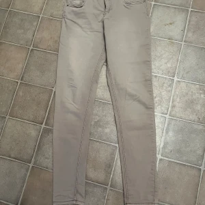 Beige byxor från H&M - Säljer ett par snygga beige byxor från H&M i storlek 38. De är tillverkade av 72% bomull, 26% polyester och 2% elastan, vilket gör dem både bekväma och stretchiga. Perfekta för vardagsbruk!