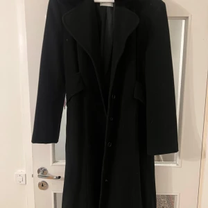 Svart lång kappa  - En lång svart kappa i lyxigt och tungt material. Använd ett få antal gånger och passar perfekt till det kalla vädret. Köpter för 2500 men säljer för mindre än halva priset. Skriv om du vill ha fler bilder. 