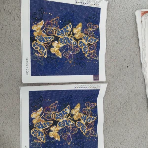 Broderimönster med fjärilar - Två diamond painting med vackra fjärilar i guld och blått. Mönstren är 30 x 30 cm stora och har en mörkblå bakgrund som framhäver de gyllene detaljerna. En för 35 två för 50