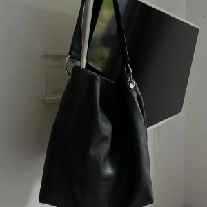 Svart axelväska med dragkedja - Säljer en stilren svart axelväska i konstläder. Väskan har en praktisk dragkedja som passar perfekt till skola eller jobb. Får plats med macbook 13’ 