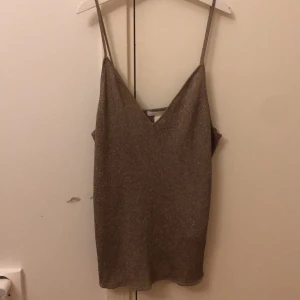Glittrig linne från H&M - Säljer ett snyggt glittrigt linne från H&M i storlek L. Linnet har smala axelband och en v-ringad design, perfekt för festliga tillfällen. Det är i en neutral färg som passar till det mesta.