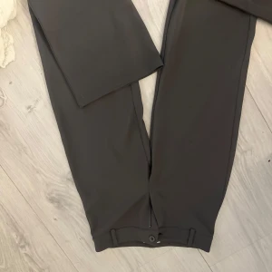 Grå kostymbyxor - Snygga grå kostymbyxor med en klassisk design. Byxorna har en rak passform och är perfekta för en stilren look. De är tillverkade i ett material som ger en elegant känsla. Lågmidjade