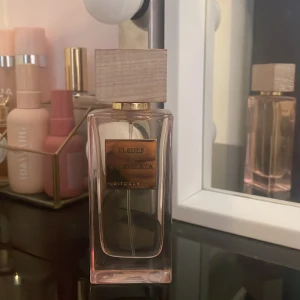 Parfym från Rituals - Elegant parfymflaska från Rituals med en stilren design. Flaskan har en rektangulär form med en träliknande kork och en etikett i guld. Doften heter 'Fleurs de l'Himalaya'. Perfekt för den som söker en sofistikerad och unik doftupplevelse.