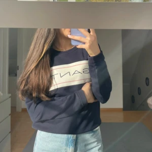 Mörkblå sweatshirt från Gant - Säljer en snygg mörkblå sweatshirt från Gant med ett vitt och rött tryck på bröstet. Tröjan har långa ärmar och en klassisk rund halsringning