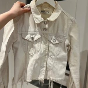 Vit jeansjacka från Gina tricot  - Snygg jeansjacka i storlek S. Jackan har en croppad design med fransig nederkant och knappar framtill. Perfekt för en avslappnad stil. Har inte använt denna på 2 år därav säljer jag den. Normalt använd🤍