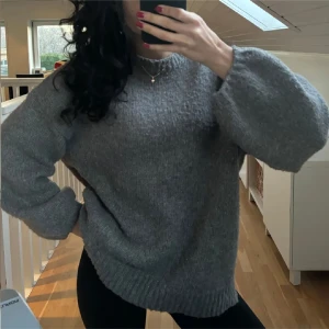 Grå stickad tröja - Mysig grå stickad tröja med långa ärmar och ribbade muddar. Perfekt för kyliga dagar.