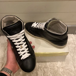 Svarta sneakers från Maison Margiela - Snygga svarta sneakers från Maison Margiela i skinn med vita snören och en klassisk design. Perfekta för en stilren look.