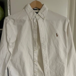 skjorta från Ralph Lauren - Snygg vit skjorta från Ralph Lauren med klassisk krage och broderad logotyp på bröstet. Skjortan har en slim fit passform och knappar framtill. Perfekt för en stilren look.