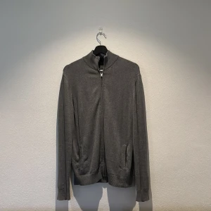 Grå kofta från Pier One - Säljer en stilren grå kofta från Pier One med dragkedja framtill. Koftan har långa ärmar och ribbade muddar vid ärmslut och nederkant. Perfekt för lager-på-lager under kyligare dagar.