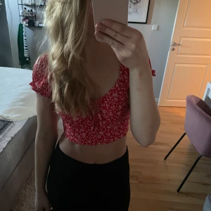 Röd blommig croppad topp - Säljer en söt röd croppad topp från Nelly med vita blommor. Toppen har korta ärmar och en knytning framtill som ger en fin detalj. Perfekt för sommardagar! Använd fåtal gånger och har mycket bra skick. 
