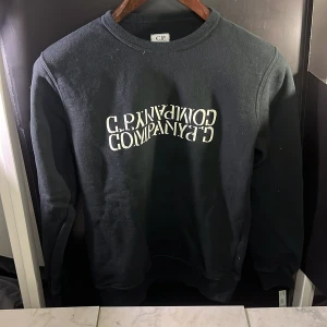 Svart sweatshirt från C.P. Company - Säljer en svart sweatshirt från C.P. Company med tryck på framsidan. Tröjan har en klassisk rund hals och långa ärmar. Perfekt för en avslappnad stil. Hör av er vid minsta fundering🙌