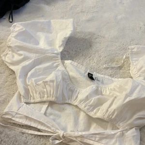 Vit kortärmad topp från H&M Divided - Säljer en söt vit topp från H&M Divided med korta puffärmar och knytning framtill. Perfekt för sommardagar och kan enkelt matchas med olika outfits.🩷