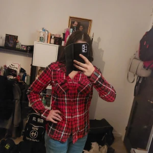 Röd och svart rutig skjorta - Snygg röd och svart rutig skjorta med knappar framtill. Skjortan har långa ärmar och en klassisk krage. Perfekt för en avslappnad stil.