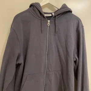 Grå zip-hoodie från Weekday - Säljer en stilren grå/lila hoodie från Weekday i storlek S, men passar även M. Den har en dragkedja framtill och en  huva med snören. Perfekt för en avslappnad look.