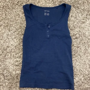 Mörkblå ribbad linnetopp från Esmara - Säljer en mörkblå ribbad linnetopp från Esmara. Toppen har en rund halsringning och tre knappar framtill. Passar s/m