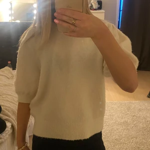 Vit stickad tröja - Säljer en mysig vit stickad tröja med korta ärmar. Perfekt till vardagen. Tröjan har en rund halsringning och en bekväm passform.