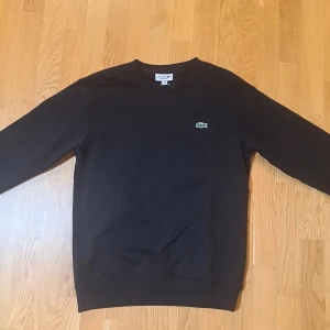 Svart tröja från Lacoste - Säljer en stilren svart tröja från Lacoste. Tröjan har en normal passform och långa ärmar. Ny pris 1.300kr. Kom även med byten