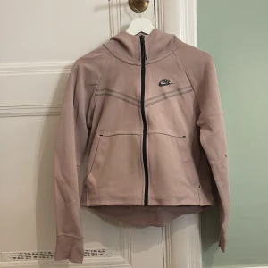 Beige hoodie från Nike - Säljer en beige hoodie från Nike med dragkedja och huva. Jackan har långa ärmar och en stilren design med Nike-logga på bröstet. Perfekt för en avslappnad stil.
