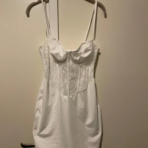 Vit klänning med spetsdetaljer - HELT NY!!  Skitsnygg vit kortare klänning med smala axelband och vacker spetsdetalj på överdelen. Klänningen har en figurnära passform och har riktigt mjukt, strechigt material. Köpte för att ha på halloween men den kom för sent så den är helt oanvänd.